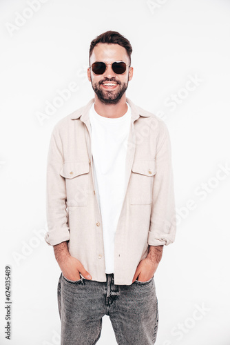 Portrait of handsome smiling stylish hipster lambersexual model. Sexy man dressed in white T-shirt and jeans. Fashion male isolated on white background in studio. In sunglasses