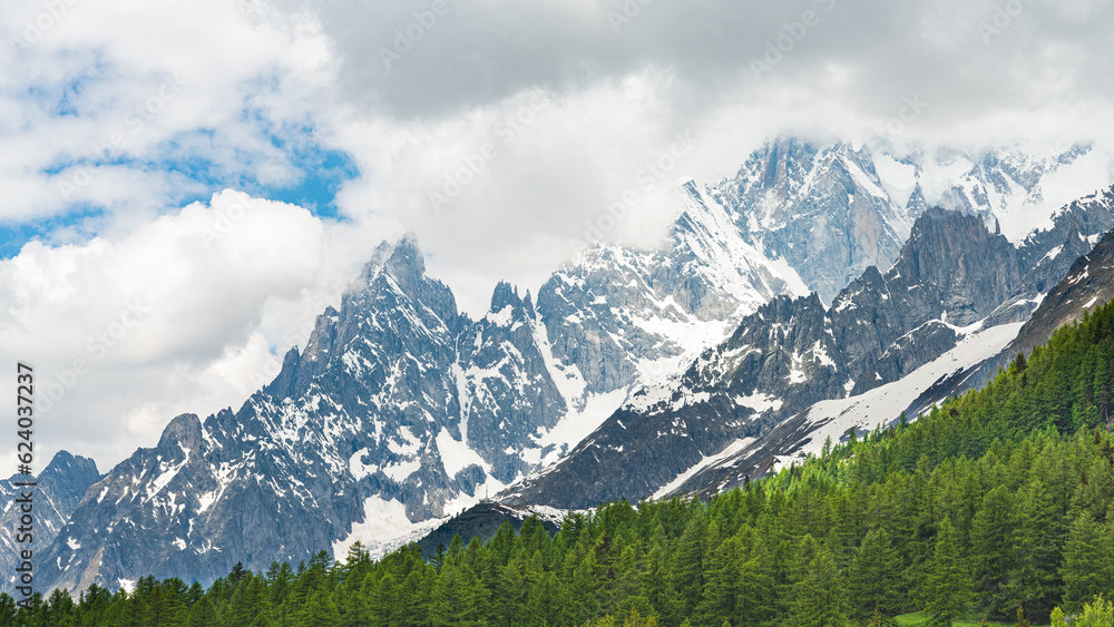 The famous Monte Bianco's peak (White Mountain) covered by dark clouds, in Aosta Valley, Italy. Green pine forest in the foreground. Clouds on the background.