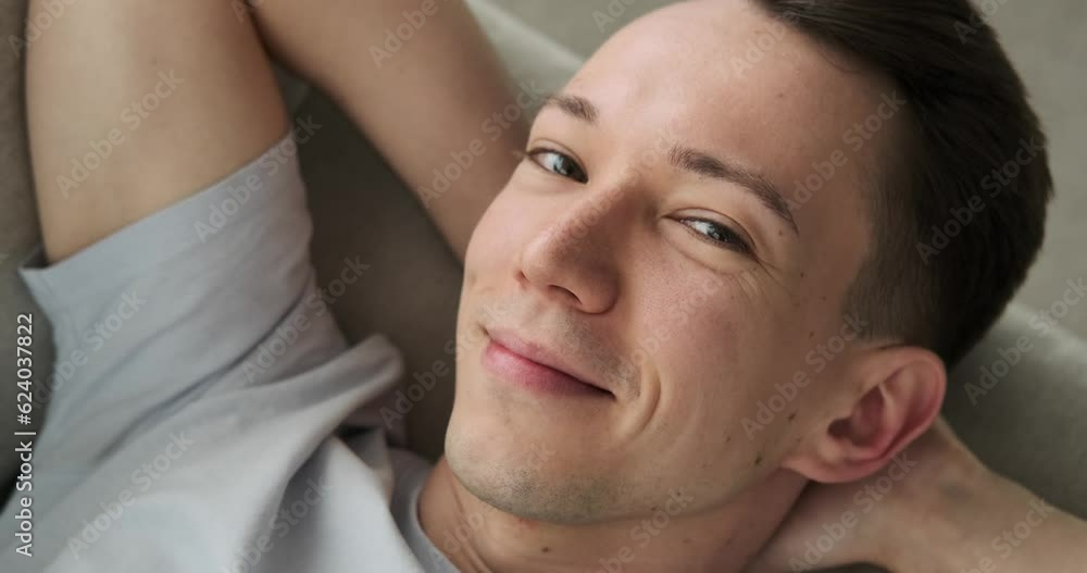 a Caucasian man lying comfortably on the couch, his eyes fixed on the camera, and a beaming smile adorning his face. Showing pure happiness and contentment. a Caucasian man lying comfortably on the couch, his eyes fixed on the camera, and a beaming smile adorning his face. Showing pure happiness and contentment.