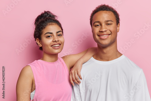 Canvastavla Pair of young happy smiling African male and European female standing close to each other in centre on pink background wearing sporty clothes