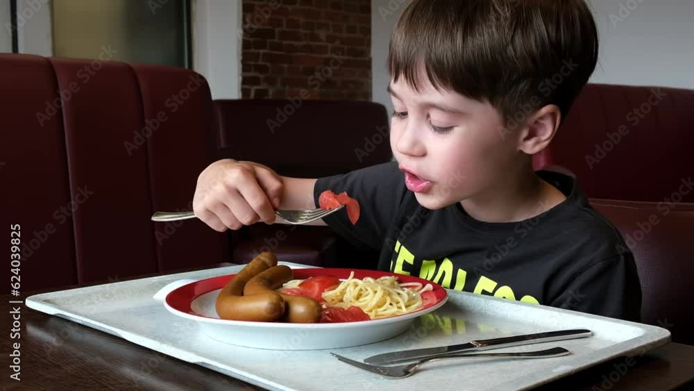 A 7 year old boy eats pasta with tomato then bites into a sausage and spit it out. Tasteless food. Lunch in canteen. Plate on tray. A good appetite. Untasty meal. Copy space. Close-up. Dinner. Hungry. A 7 year old boy eats pasta with tomato then bites into a sausage and spit it out. Tasteless food. Lunch in canteen. Plate on tray. A good appetite. Untasty meal. Copy space. Close-up. Dinner. Hungry.