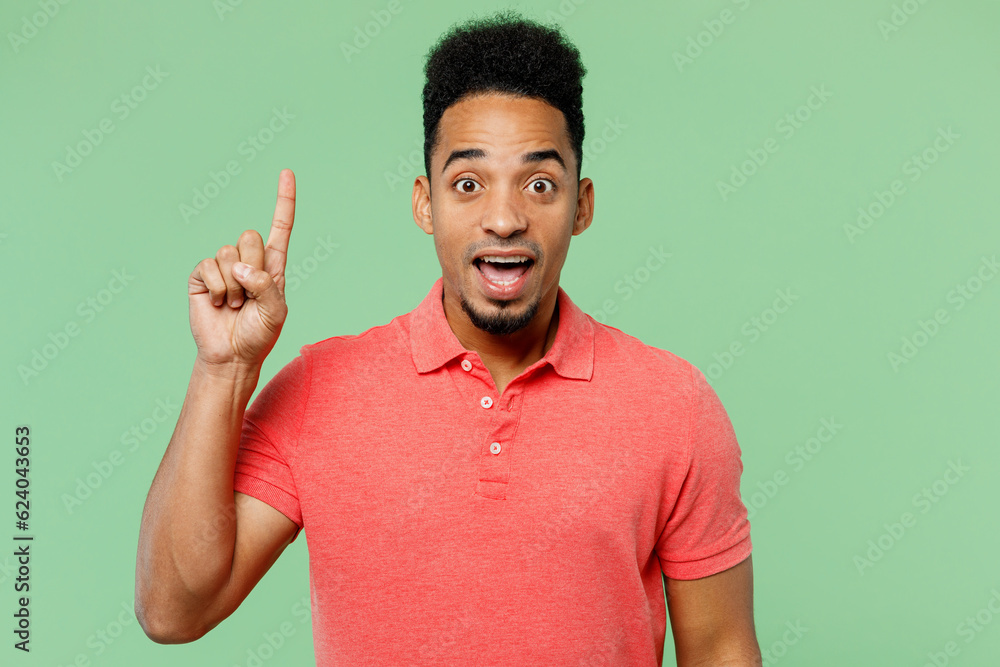 Young insighted smart proactive man of African American ethnicity he wearing pink t-shirt hold index finger up with great new idea isolated on plain pastel light green background. Lifestyle concept. Young insighted smart proactive man of African American ethnicity he wearing pink t-shirt hold index finger up with great new idea isolated on plain pastel light green background. Lifestyle concept.