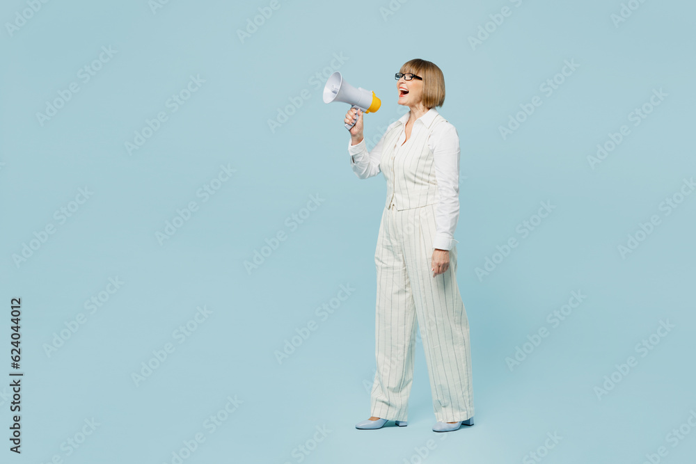 Full body side view employee business woman 50s wear white classic suit glasses formal clothes hold in hand megaphone scream isolated on plain pastel light blue background. Achievement career concept. Full body side view employee business woman 50s wear white classic suit glasses formal clothes hold in hand megaphone scream isolated on plain pastel light blue background. Achievement career concept.