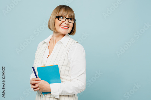 Side view happy employee business woman 50s wear white classic suit glasses formal clothes hold in hand notebook look aside isolated on plain pastel light blue background. Achievement career concept.