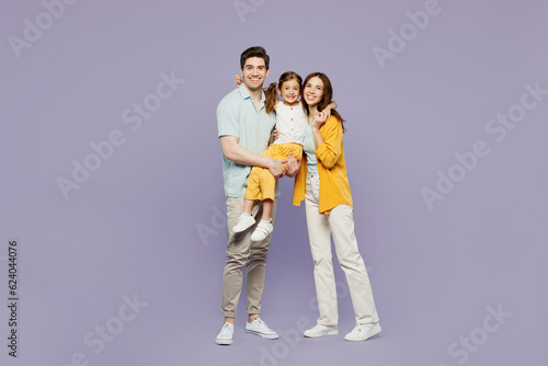 Full body young happy parents mom dad with child kid girl 6 years old wears blue yellow casual clothes hold daughter hugging cuddling embrace isolated on plain purple background. Family day concept.