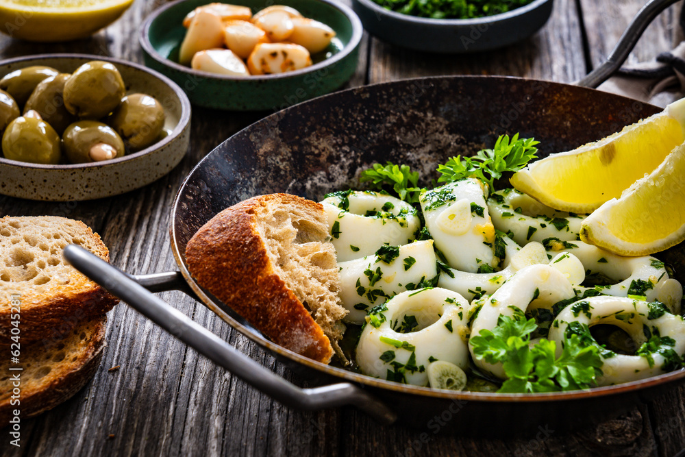 Fried calamari rings with garlic, lemon and parsley in pan on wooden table
Fried calamari rings with garlic, lemon and parsley in pan on wooden table