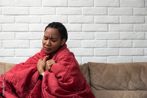 Fotografia Sick young african woman feeling cold covered with blanket sit on sofa, ill blac