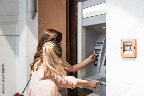 Εκτύπωση καμβά Two beautiful tourists female withdrawing the money from a bank card using ATM machine at the city center