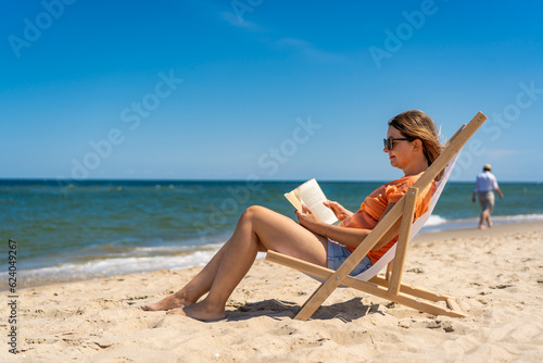 Woman relaxing on beach reading book sitting on sunbed
 #624049267