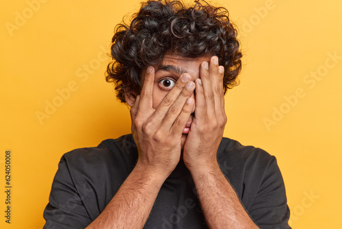 Cuadro en lienzo Photo of shocked curly haired Hindu man hides face with hands peeks through fing