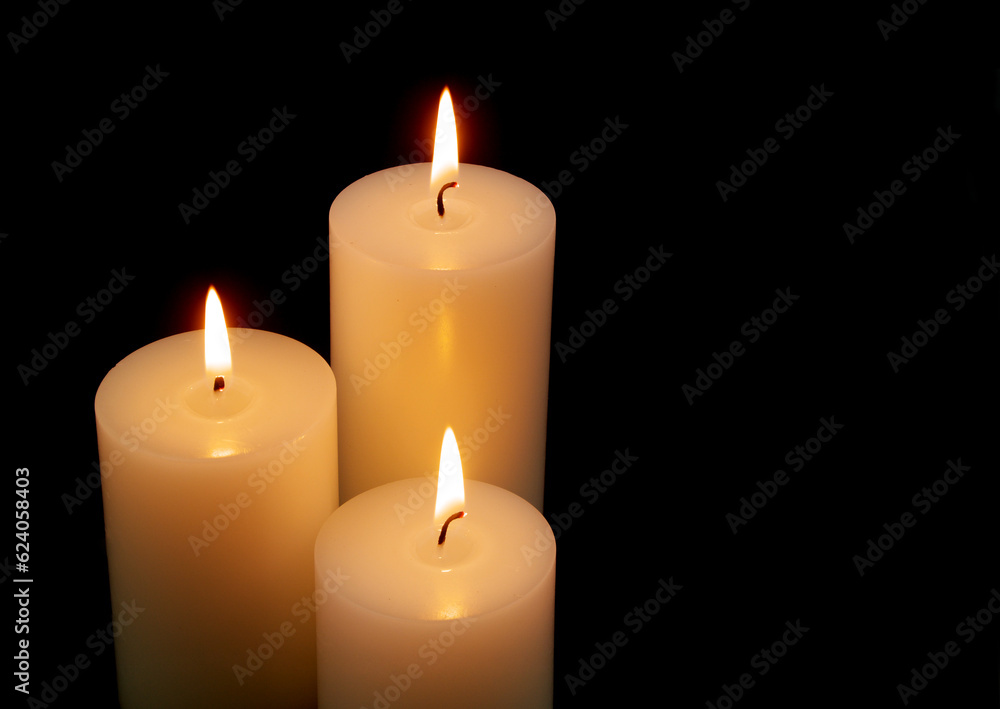 White candles with different size burning on black background with space for text.