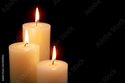 White candles with different size burning on black background. Copy space for text.