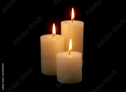 Three white candles with different size burning on black background.