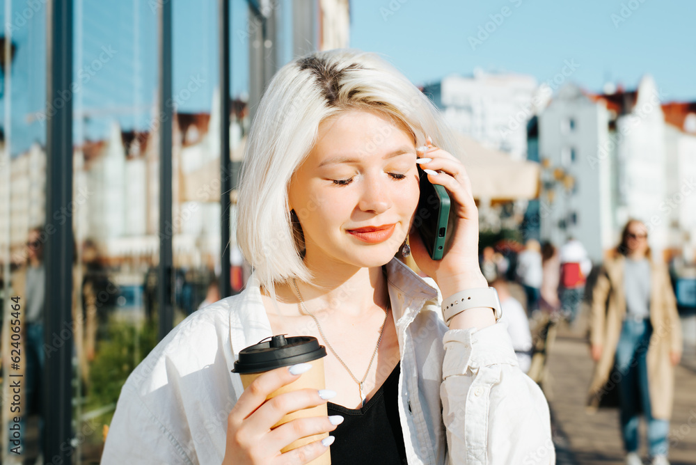 Φωτογραφία Young pretty woman listening to pleasant conversation on smartphone while walking with a disposable cup of coffee outdoors on a sunny day