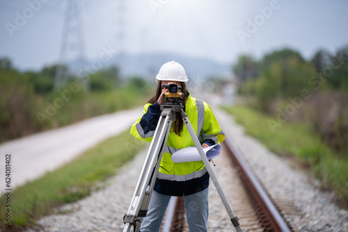 Surveyor engineers team wearing safety uniform,helmet and blueprint document checking inspection by theodolite to measurement position on railway construction site is industry transportation concept.
