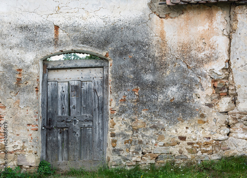 Weathered grey wooden door in old dilapidated stone wall.