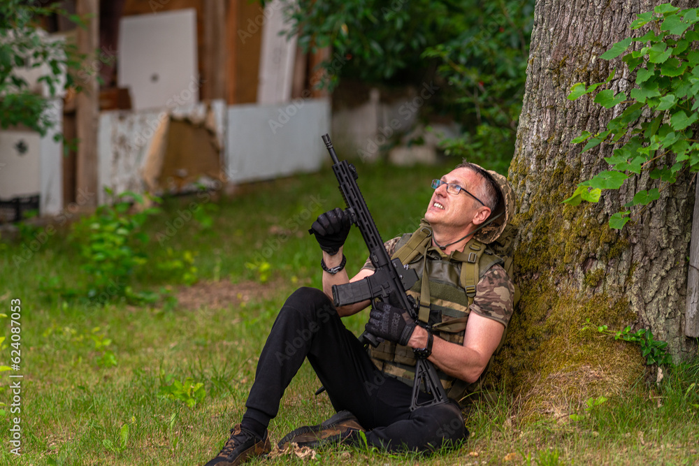 A man with a gun looks up while sitting under a tree