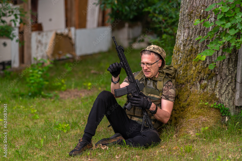 A soldier checks a weapon while sitting under a tree