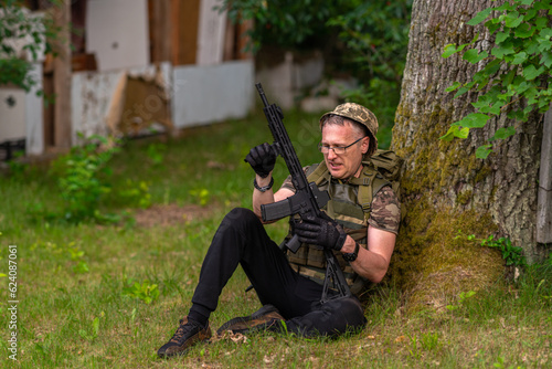Obraz na płótnie A soldier checks a weapon while sitting under a tree w salonie