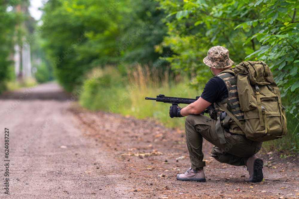 Man with AR crouched on the side of the road