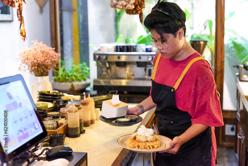 Vietnamese young waitress serving sweet waffles with banana and cream in a cafe