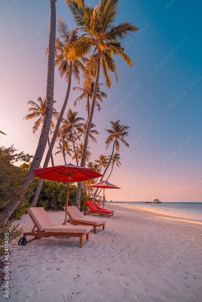 Beautiful tropical sunset coast, two sun beds chairs umbrella under palm trees. Closeup white sand, sea view horizon colorful twilight sky calm and relaxation. Inspire beach resort wellbeing landscape