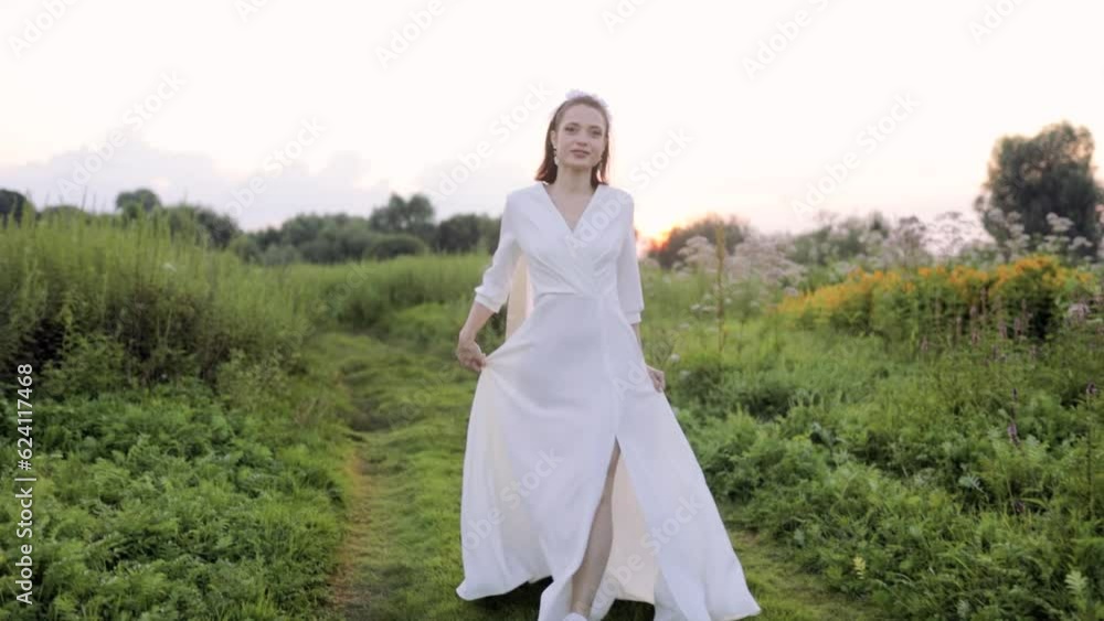 beautiful woman model in a white dress walks across the field at sunset. The concept of a free and independent woman beautiful woman model in a white dress walks across the field at sunset. The concept of a free and independent woman