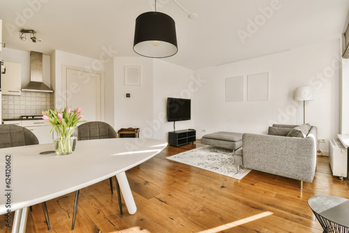 a living room with wood flooring and white walls  including a large dining table surrounded by two grey chairs
