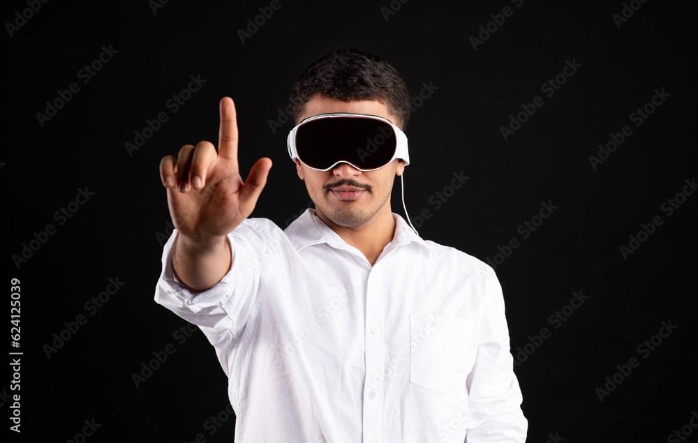Naklejka premium Metaverse concept. Modern latin man in vision pro vr glasses, trying to touch something with finger on black background