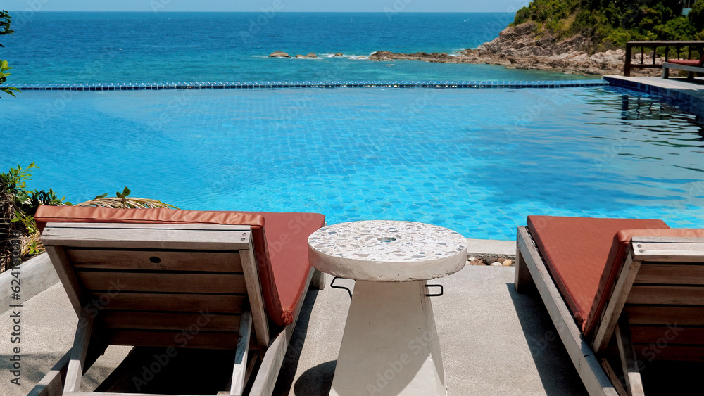 Two beach chairs and a cocktail table near a swimming pool on a sunny day. Summer vacation. Concept of relaxation and leisure. Two beach chairs and a cocktail table near a swimming pool on a sunny day. Summer vacation. Concept of relaxation and leisure.