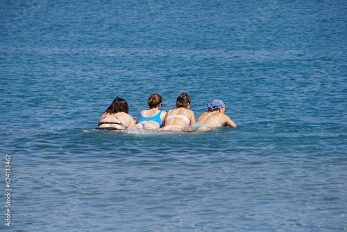 Vier Frauen von hinten auf der Luftmatratze im blauen Wasser