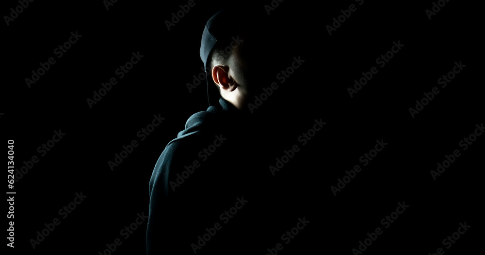 Man standing alone in the dark wearing a black hoodie and hat