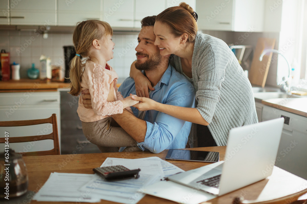Young family hugging in the kitchen while going over their bills in the morning Young family hugging in the kitchen while going over their bills in the morning