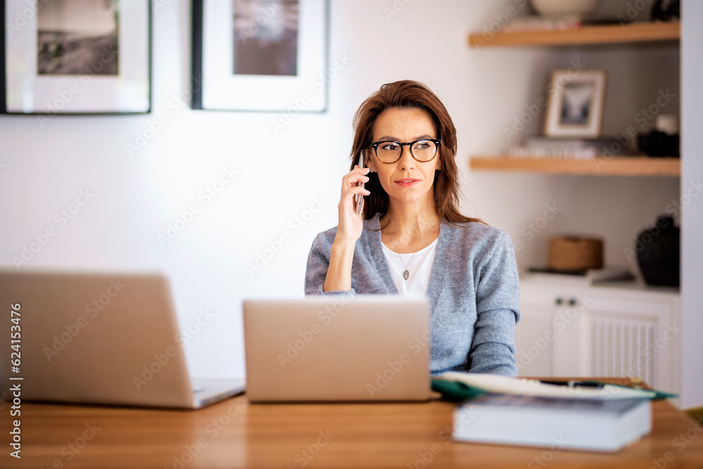 Mid aged business woman sitting at home and using laptops and having a call Mid aged business woman sitting at home and using laptops and having a call
