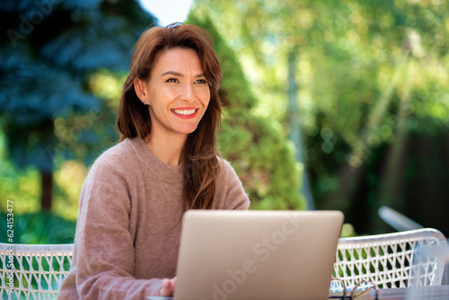 An attractive mid aged woman sitting outside and using laptop for work