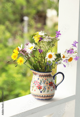 A beautiful ceramic jug with wildflowers on the railing of the summer veranda. Selective focus. 