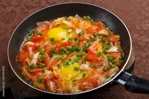 hot shakshuka in a frying pan sprinkled with green onions on a wooden board.