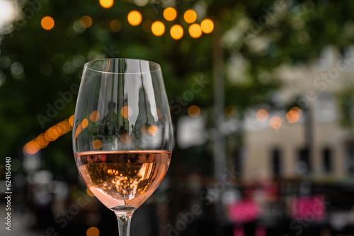 Glass of refreshing rose wine on a table of a city cafe terrace on summer evening. Street in bokeh.