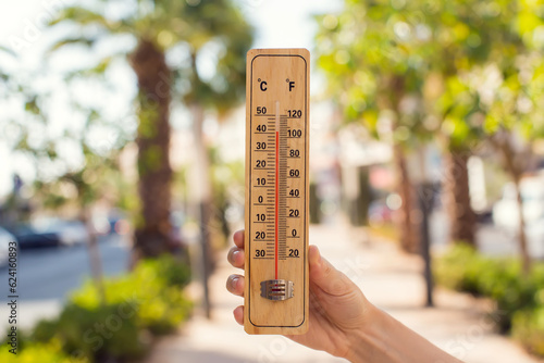 Hot weather. Thermometer in hand in front of street with trees and palms during heatwave. High temperature concept