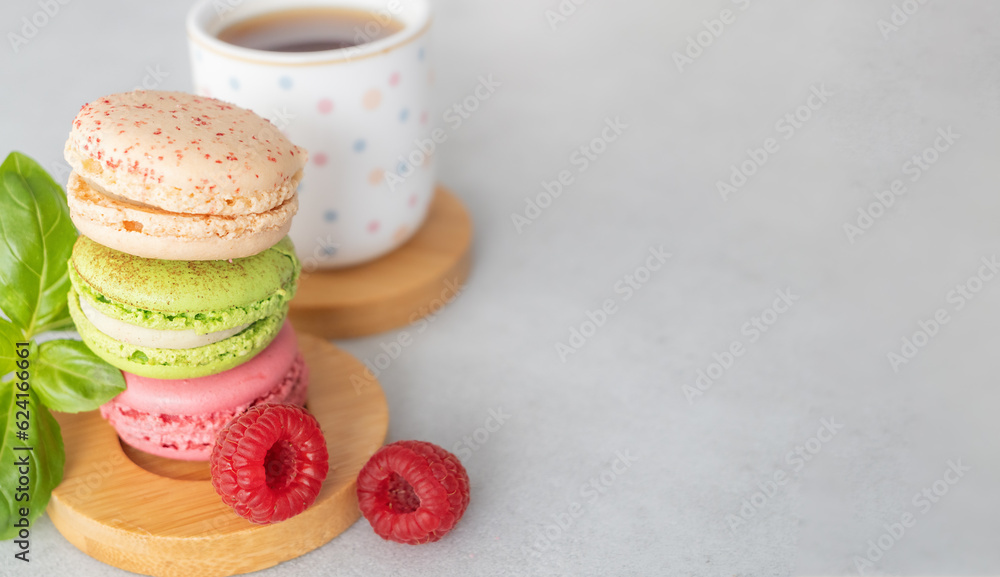French traditional cookies - macaron, French macaroon, tea cup and raspberries on a light background with copy space. Confectionery according to classic French recipes.