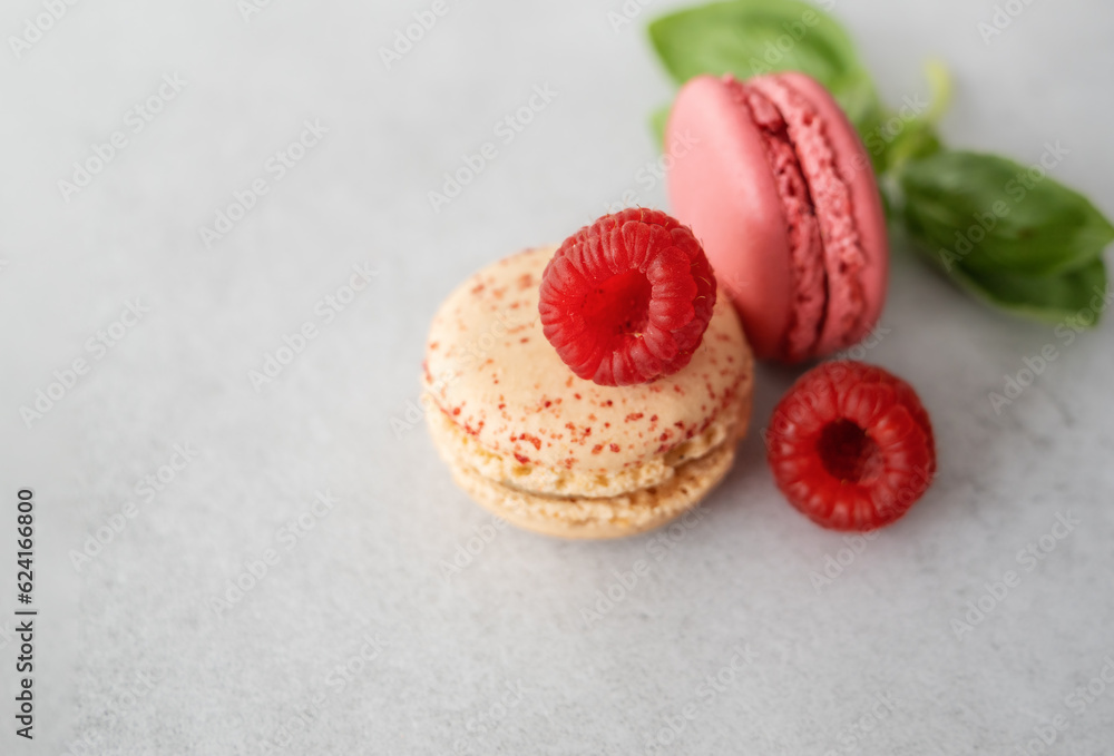 Two macaroons with berry filling and raspberries lie on a light gray background Two macaroons with berry filling and raspberries lie on a light gray background