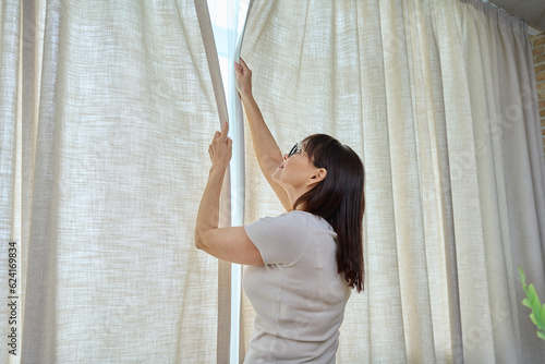 Konstfotografi Back view, woman closes light curtains in the living room