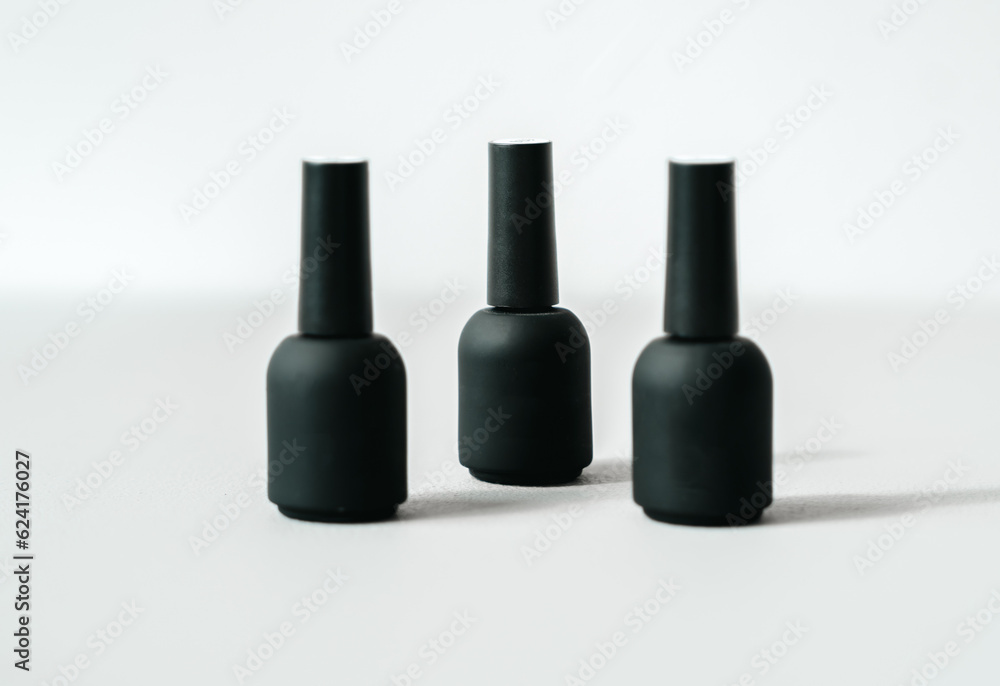 Black bottles with samples of nail polishes on white background. Professional master manicurist at beauty salon. Manicure service,hands treatments, fingers procedures Black bottles with samples of nail polishes on white background. Professional master manicurist at beauty salon. Manicure service,hands treatments, fingers procedures