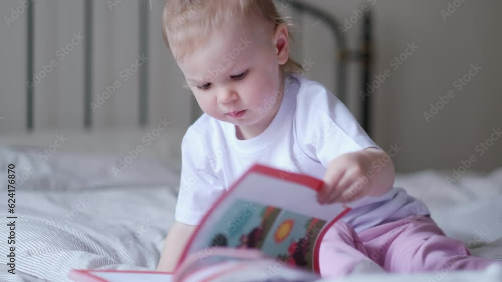 little baby girl reading, looking at pictures in book on bed at home, An inquisitive baby wants to read new fairy tale little baby girl reading, looking at pictures in book on bed at home, An inquisitive baby wants to read new fairy tale
