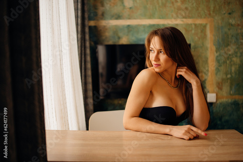 Portrait of a beautiful and sexy young woman in a black bustier at a table.  photo