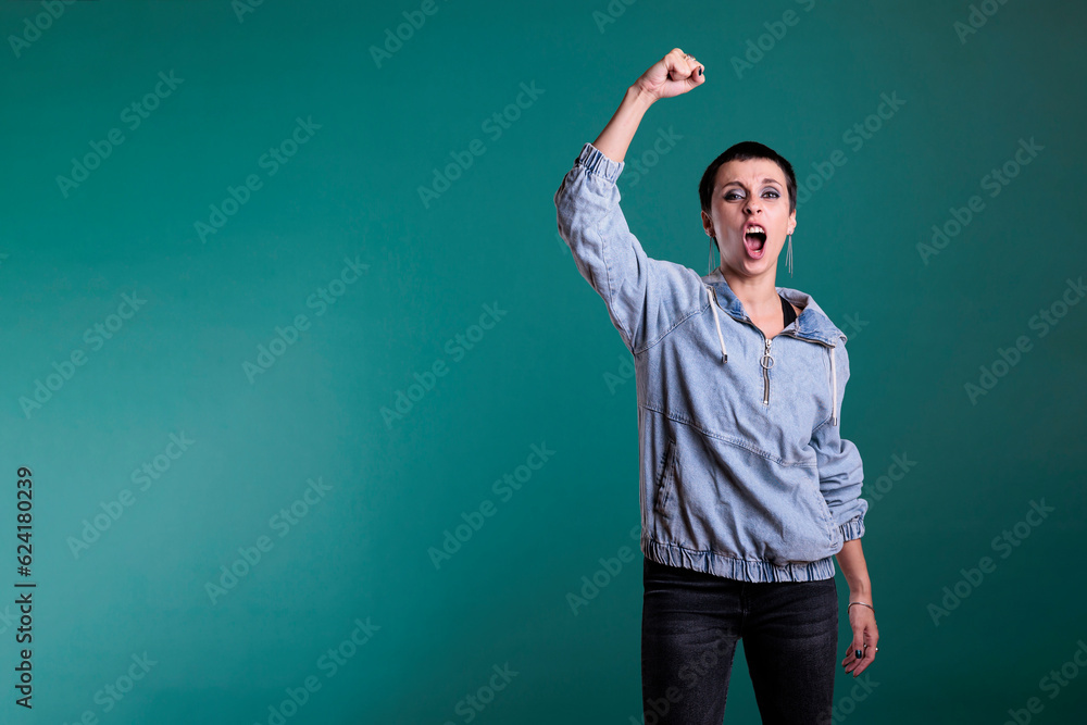 Excited woman celebrating good scoring of soccer championship, cheering football team while standing in studio with isolated background. Happy female raising hands after winning the competition