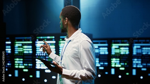 African american supervisor in server farm using tablet to find firewall misconfigurations affecting rackmounts performance and connectivity, leading to slow data transfer rates photo