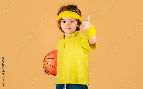 Active sport lifestyle. Basketball game. Little sporty kid with basketball ball showing thumb up. Child boy with ball. Kid activity. Little basketballer in sportswear with basketball. Sport equipment. photo