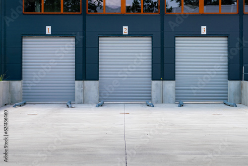 Three roller garage doors next to each other. Numbers on the doors indicate the location for transportation trucks. Loading zone in front of an industry building. Industrial background as mockup.