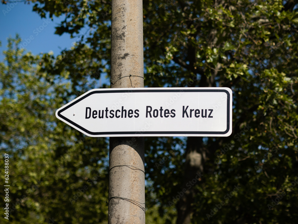 Guiding street sign with the letters Deutsches Rotes Kreuz (German Red Cross). The arrow is pointing to the left. The organisation is providing health care services like hospitals, emergengy services.